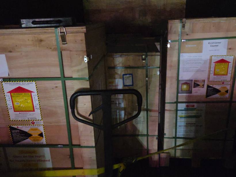 Tall wooden crates with shock and tilt indicator labels banded together inside the truck with a pallet jack in front