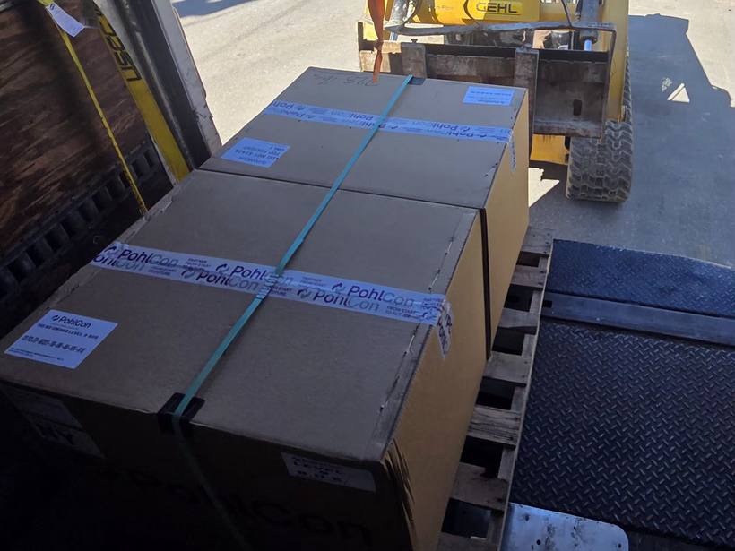 Two strapped cartons on a wooden pallet inside the box truck with a skid steer waiting on the street behind